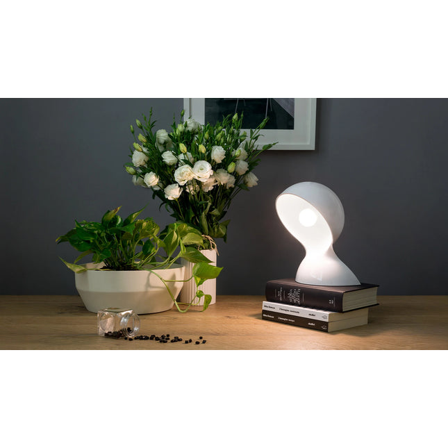 Lampe Dalù blanche allumée sur une pile de livres, près d’un bouquet de fleurs blanches