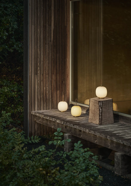 Plusieurs lampes VL 45 Radiohus Portable allumées sur un banc en bois, de nuit, en extérieur