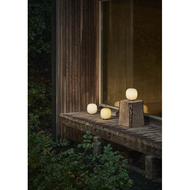 Plusieurs lampes VL 45 Radiohus Portable allumées sur un banc en bois, de nuit, en extérieur